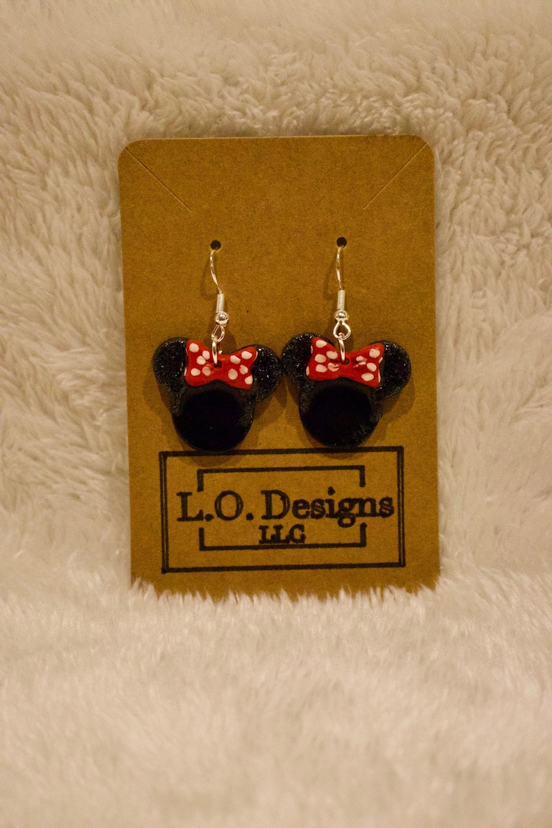 May include: A pair of black and red glitter Minnie Mouse earrings with white polka dots on the bow. The earrings are on a brown card with the text "L.O. Designs LLC".