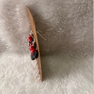May include: A pair of dangle earrings with black and red beads. The earrings are on a brown card.