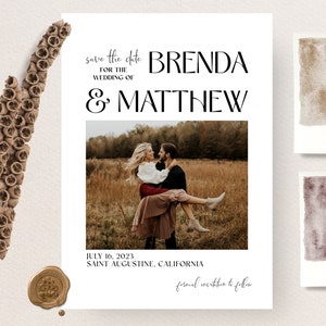 Op de afbeelding: Een trouw save-the-date kaart met de namen BRENDA & MATTHEW, een foto van een stel en de datum 16 juli 2023. De kaart heeft een minimalistisch ontwerp met aquarel stalen en een zegel.