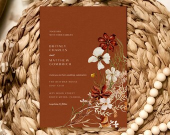 May include: A wedding invitation with a rust-colored background and a floral design featuring white and red flowers. The invitation text reads "Together with their families, Britney Charles and Matthew Gombrich invite you to their wedding celebration, The Heitman House Golf Club, 1855 Wood Street, Forth Myers, Florida, reception to follow."