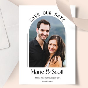 Op de afbeelding: Save the date-kaart met een foto van een stel voor een bergketen. De tekst luidt "Save Our Date" in een cirkel boven de foto en "Marie & Scott" onder de foto. De datum en locatie staan onder de namen: "July 16, 2023 Denver, Colorado".