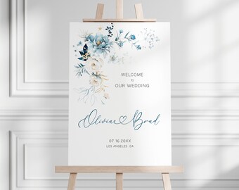 May include: A wedding welcome sign with a blue and white floral design. The sign says "Welcome to our wedding" and features the names "Olivia & Brad" with a heart symbol. The date "07 16 20XX" and location "Los Angeles CA" are also included.