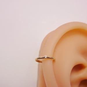 May include: A gold hoop earring with a small clear gemstone set in the center.