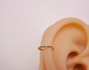 May include: A gold hoop earring with a small clear gemstone set in the center.