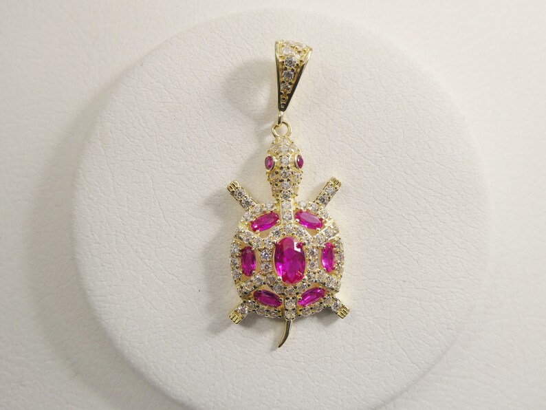 May include: Gold-tone turtle pendant with pink and white cubic zirconia stones.