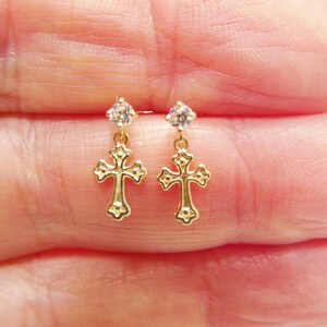 May include: A pair of gold cross earrings with a small clear rhinestone dangling from each cross.