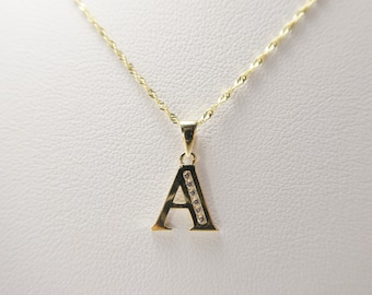 Puede incluir: Un collar de cadena de oro con un colgante en forma de la letra A. La letra está engastada con pequeñas piedras transparentes.