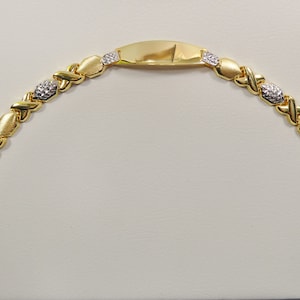 May include: A gold bracelet with a flat, rectangular tag in the center. The bracelet is made of interlocking oval links, some of which are set with small, clear stones.