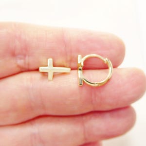 May include: A pair of gold earrings, one is a small hoop and the other is a small cross.