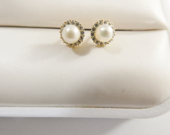 May include: A pair of gold earrings with a pearl and clear stones in a circular setting.