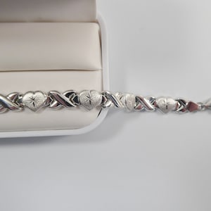 May include: A silver bracelet with a heart-shaped design. The bracelet is made of interlocking links and has a clasp closure.