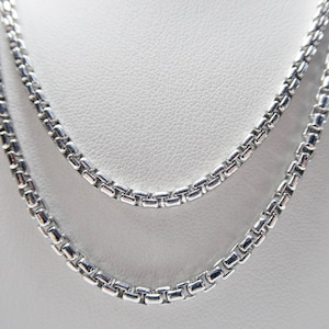 May include: Two silver chain necklaces layered on a white background. The chains are made of small, square-shaped links.
