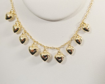 May include: A gold chain necklace with multiple dangling heart charms. The necklace is on a white background.