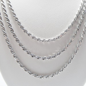 May include: Three silver-colored rope chains displayed against a white background. The chains are of varying lengths, each with a twisted rope design. The jewelry is presented in a studio setting, highlighting the reflective quality of the metal.