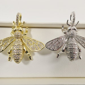 May include: Two bee-shaped pendants, one gold and one silver, with clear crystal accents. Both pendants feature detailed wings and a three-dimensional body.