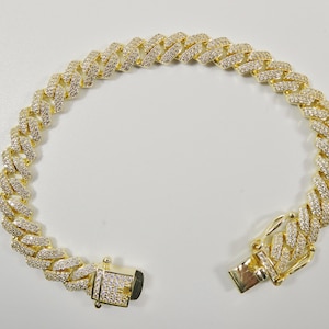 May include: A gold chain bracelet with a clasp closure. The chain is made of small, interlocking links and is covered in clear cubic zirconia stones.