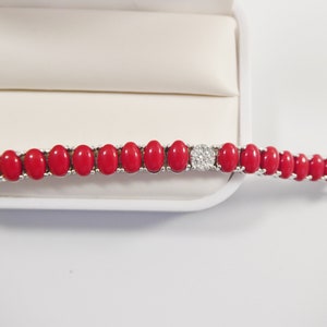 May include: A red coral bracelet with a silver clasp and a cluster of clear stones in the center.