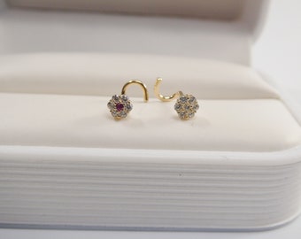May include: Two gold nose rings with a small red gemstone in the center of a flower design surrounded by clear gemstones.