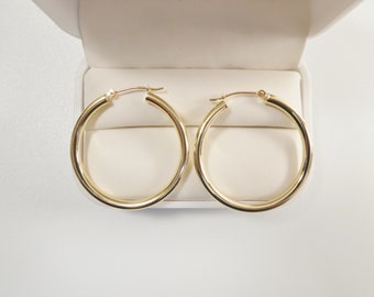 May include: A pair of gold hoop earrings in a white box. The earrings are simple and classic, with a smooth, polished finish.