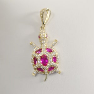 May include: A gold-tone pendant featuring a turtle design with pink and white cubic zirconia stones.