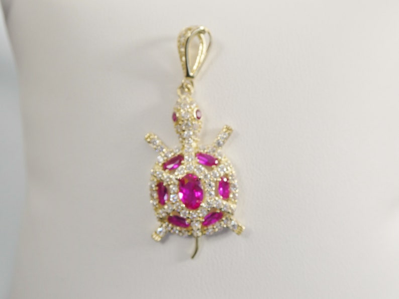 May include: A gold-tone pendant featuring a turtle design with pink and white cubic zirconia stones.