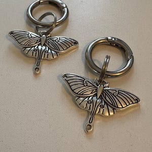 May include: Two silver keyrings with a detailed silver moth charm attached to each. The keyrings have a silver split ring and a silver lobster clasp.