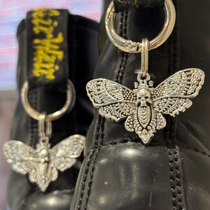 May include: Black leather boots with silver skull and butterfly charms attached to the laces. The charms are detailed with intricate designs.