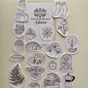 May include: A selection of white fabric patches featuring black line drawings of autumn motifs such as a pumpkin, leaf, and spiderweb. The text "Stick and Stitch pack Autumn" is displayed on a white card.