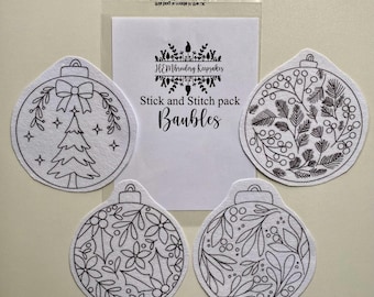 May include: A pack of stick and stitch baubles with various black and white designs. The designs include a Christmas tree, floral patterns, and botanical elements. The packaging includes the text "HEMbroidery Keepsakes" and "Stick and Stitch pack Baubles."
