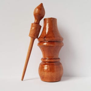 May include: A wooden bottle stopper with a matching wooden dowel. The bottle stopper is brown and has a rounded shape. The dowel is long and thin.