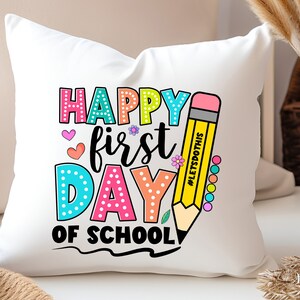 May include: White square pillow with a colorful "Happy First Day of School" design. The text is in various colors and fonts, with a large yellow pencil graphic. The pencil has the text "#LETSDOTHIS" on it.