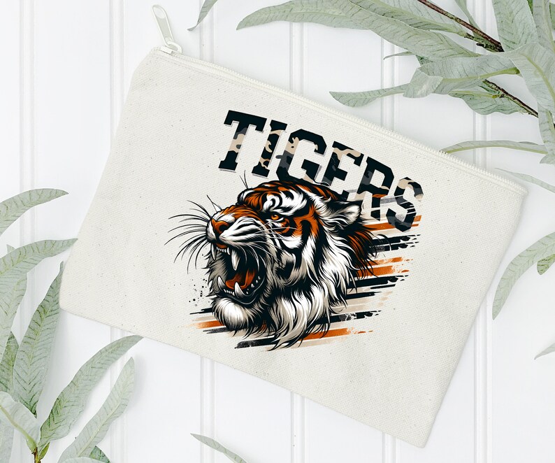 K&ouml;nnte beinhalten: Eine wei&szlig;e Canvas-Rei&szlig;verschlusstasche mit einer Grafik eines br&uuml;llenden Tigers mit orangefarbenen und schwarzen Streifen. Der Text "TIGERS" ist in Schwarz &uuml;ber dem Tiger gedruckt.