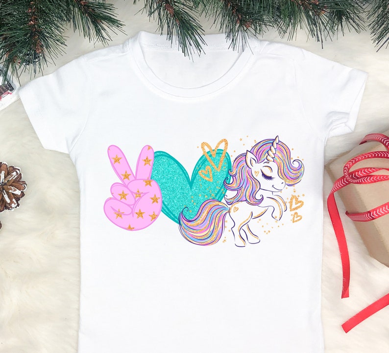 May include: White t-shirt with a pink peace sign, a teal heart, and a rainbow unicorn with gold glitter accents. The text "Peace Love Unicorn" is printed on the shirt.