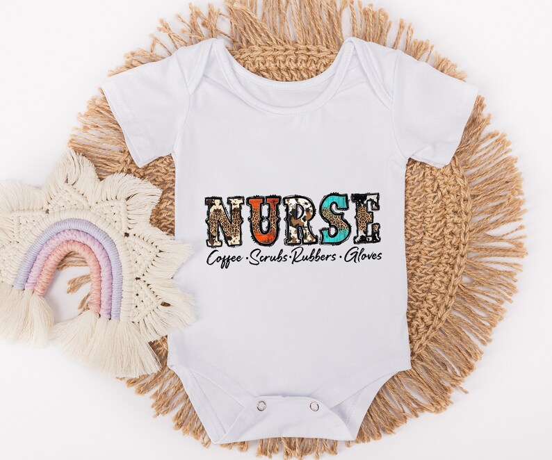 May include: White baby onesie with the word "NURSE" in colorful patterned letters. The text "Coffee. Scrubs. Rubbers. Gloves" is printed below the word "NURSE".
