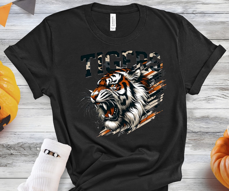 K&ouml;nnte beinhalten: Schwarzes T-Shirt mit einem Tigerkopf-Motiv und dem Wort "TIGERS" in einem Tarnmuster dar&uuml;ber.