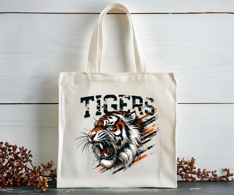 K&ouml;nnte beinhalten: Eine wei&szlig;e Canvas-Tragetasche mit einem Tiger-Motiv und dem Wort "TIGERS" in Schwarz gedruckt. Der Tiger ist orange, schwarz und wei&szlig; mit einem wilden Ausdruck.