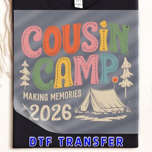 May include: Black t-shirt with a colorful graphic that reads "COUSIN CAMP" in stitched letters. Below, it says "MAKING MEMORIES 2026" with a tent and trees illustration. The bottom text reads "DTF TRANSFER".