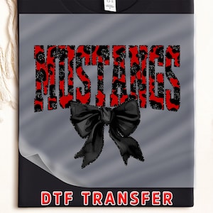 May include: Black t-shirt with a gray overlay featuring the word "MUSTANGS" in red leopard print. A black bow is below the word. The text "DTF TRANSFER" is at the bottom in a red rectangle.