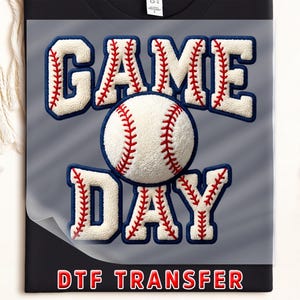 May include: A black t-shirt with a baseball-themed design. The words "GAME DAY" are in white, fluffy letters with red stitching and blue outlines, with a baseball in the center. The text "DTF TRANSFER" is in red at the bottom.
