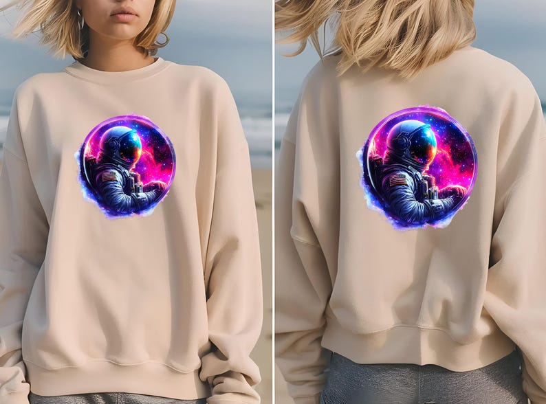 Pode incluir: Camisola bege com um gr&aacute;fico vibrante de um astronauta numa cena espacial. O astronauta est&aacute; dentro de uma moldura circular com um fundo de nebulosa colorida. O design &eacute; repetido na frente e atr&aacute;s da camisola.