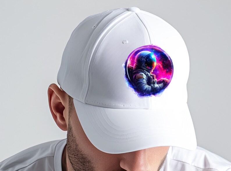 Pode incluir: Bon&eacute; de beisebol branco com um gr&aacute;fico circular de um astronauta no espa&ccedil;o. O astronauta usa um capacete e um traje azuis, em um fundo de nebulosas rosa, roxas e azuis. O bon&eacute; tem um design cl&aacute;ssico de seis pain&eacute;is.