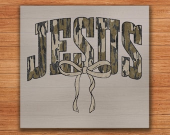 May include: A wood sign with the word "JESUS" in a camouflage pattern with a white bow underneath.