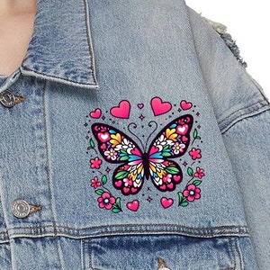 May include: A blue denim jacket with a colorful butterfly patch. The butterfly is surrounded by pink hearts and flowers.