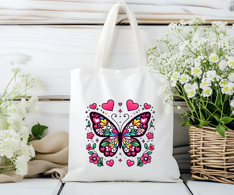 May include: White canvas tote bag with a colorful butterfly design and pink hearts. The butterfly has black wings with colorful details and is surrounded by pink hearts and flowers.