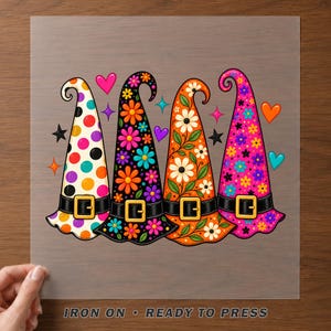 May include: A heat transfer design featuring four tall, pointed hats with black belts and gold buckles. The hats display colorful patterns including polka dots, vibrant floral prints, and leafy vines, accented by small hearts and star shapes.