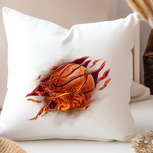 May include: White pillow with a basketball on fire bursting through the fabric. The basketball is orange and brown with flames in shades of orange and yellow.