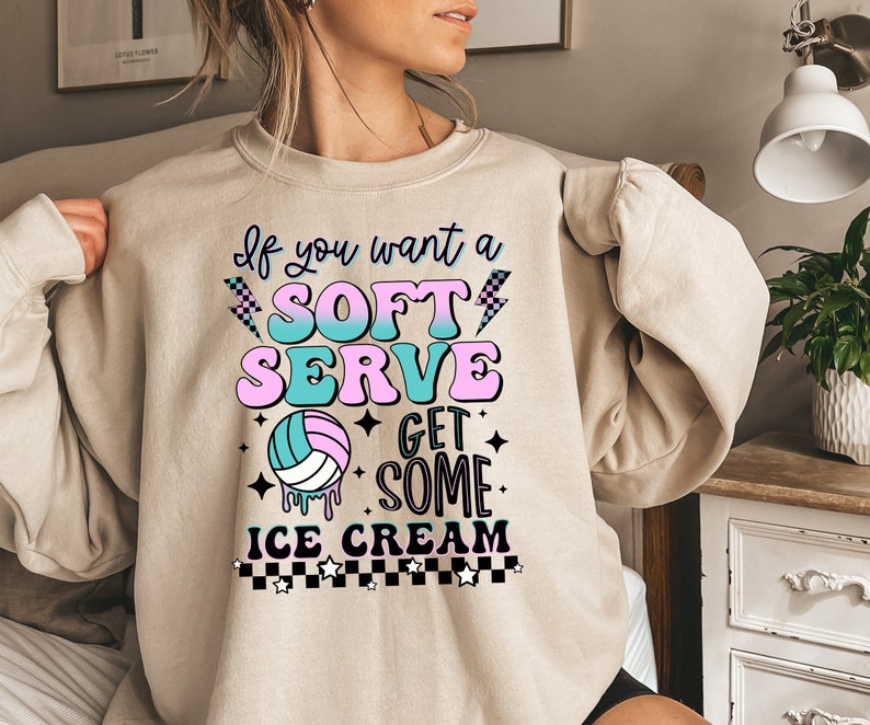 Pode incluir: Uma camisa de moletom bege com uma estampa gr&aacute;fica que diz "Se voc&ecirc; quer um sorvete mole, pegue um sorvete". O gr&aacute;fico inclui uma bola de v&ocirc;lei, raios, estrelas e um padr&atilde;o xadrez.