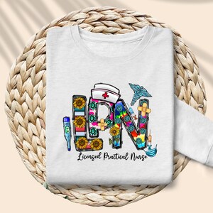 Peut inclure: Sweat-shirt blanc avec un graphique color&eacute; des lettres LPN, repr&eacute;sentant une infirmi&egrave;re auxiliaire dipl&ocirc;m&eacute;e, entour&eacute; de symboles m&eacute;dicaux et de tournesols.