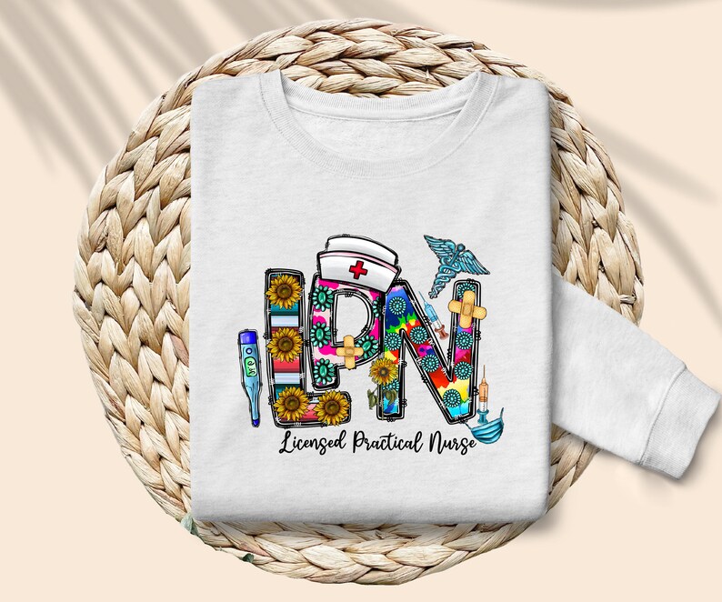 Peut inclure: Sweat-shirt blanc avec un graphique color&eacute; des lettres LPN, repr&eacute;sentant une infirmi&egrave;re auxiliaire dipl&ocirc;m&eacute;e, entour&eacute; de symboles m&eacute;dicaux et de tournesols.