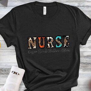 May include: Black t-shirt with the word "NURSE" in colorful patterned letters. The text "Coffee Scrubs Rubbers Gloves" is printed below the word "NURSE".